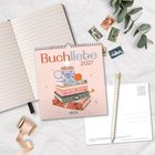 "Buchliebe 2027" steht auf einem Kalender, daneben ein Notizbuch, Stifte, Briefmarken und Eukalyptusblätter.