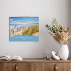 Text: "Küstenträume 2027". Ein Kalender mit einem Strandmotiv. Darunter ein Tisch mit Buch und Vase mit Trockenblumen.