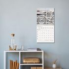 Kalenderblatt für Januar 2022, darüber ein Fahrrad vor einem Geländer. Darunter ein Regal mit Karaffe, Gläsern und Büchern.