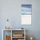 JANUAR 2027 Kalender mit Pinguinbild. Schlichter Raum mit Regal, Wasserflasche, Gläsern und Büchern.