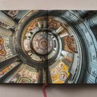 Ein aufgeschlagenes Buch zeigt den Blick in eine bemalte Deckenkuppel mit Säulen und kunstvollen Fresken.