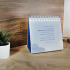 Ein Tischkalender mit Bibelversen, daneben ein kleiner Kaktus in einem weißen Topf und einige Dekosteine.