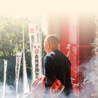 Oben steht "LAND UND LEUTE". Ein Mann mit orangefarbenem Stoff steht in Rauch vor Flaggen mit asiatischen Schriftzeichen.