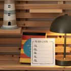 "TO-DO-LISTE", darunter fünf nummerierte Zeilen. Im Hintergrund ein Leuchtturm, eine Lampe und ein farbiges Buch.