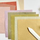 Quadratische Papiere in Rosa, Grün und Beige, mit gefalteten Blumen und einem Falzbein rechts unten.