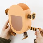 Keine Texte sichtbar. Eine Bastelarbeit aus Papier, die wie ein Cartoon-Tiger aussieht, wird von Händen gehalten.