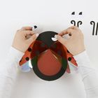 Eine Person bastelt einen Marienkäfer mit roten Flügeln und schwarzen Punkten. Hände platzieren runde Augen.