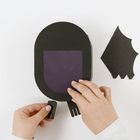 Zwei Hände legen schwarze Papierarme an eine ovale schwarze Papierform an. Daneben liegen Papierteile.