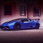 Ein blauer Sportwagen mit schwarzem Spoiler steht vor einem Gebäude mit großen Fenstern.