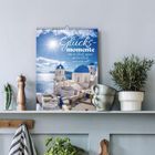 Der Text "2024 Glücksmomente. Wer an Glück glaubt, der hat Glück" ist auf einem Kalender mit Santorini-Motiv zu sehen.