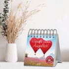 "Genieße jeden Augenblick!" Zwei Herz-Heißluftballons am Himmel, Tischkalender mit 53 Postkarten, daneben eine Vase mit Gräsern.