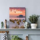 „Nord & Ostsee 2027“ steht auf einem Kalender. Strandkörbe vor einem Sonnenuntergang und Meereshorizont sind sichtbar.