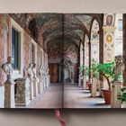 Buch doppelseitig geöffnet, zeigt einen antiken Arkadengang mit Büsten, gemusterten Wänden und Topfpflanzen.