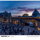 September 2027 Kalender, Open-Air-Konzert auf Schloss Burg, Menschenmenge vor Bühne in historischem Innenhof bei Abenddämmerung.