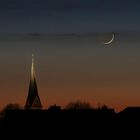 Silhouette eines Kirchturms vor einem dunkelblauen Himmel mit einer Mondsichel.