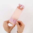 Hände halten eine hellrosa Papierkonstruktion mit ausgeschnittenen Formen.