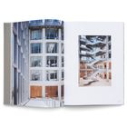 Eine offene Doppelseite eines Buches zeigt moderne Architektur mit Glasfassaden und einer geschwungenen Treppe.