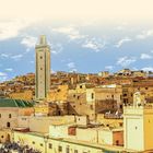 "CASABLANCA UND DIE KÖNIGSSTÄDTE" vor blauem Himmel, im Hintergrund historische Gebäude und ein hoher Turm.