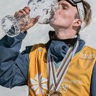 2022: Und ich bin noch lange nicht fertig! Skifahrer trinkt aus riesigem Pokal, trägt Gelb und Medaillen.