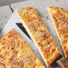 Fladenbrot-Dreiecke mit Sesam bestreut, auf hellem Holzbrett angeordnet, darunter ein Messer.