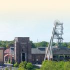 "IM ZENTRUM DES KOHLENPOTTS" über einem alten Industriegebäude mit Fördertürmen und vielen Menschen und Autos.