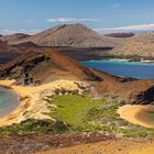 Ein türkisblaues Meer umgibt eine felsige, vulkanische Landschaft mit braunen Hügeln und grünem Bewuchs.