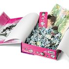 Ravensburger Puzzle-Box zeigt Illustration eines Paares. Links Text über Olga Andryienko, daneben Skizzen von Brille und Buch.