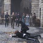 Ein Zeitungsjunge hält ein Schild mit "Disaster" hoch. Szene im viktorianischen Stil; Polizist hält Person am Boden. Passanten schauen zu.