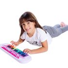 Ein Mädchen liegt auf dem Boden und spielt auf einem bunten Spielzeugkeyboard. Sie trägt ein weißes T-Shirt mit Schmetterling.