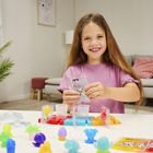 Ein Mädchen spielt lächelnd mit bunten Figuren und Formen an einem Tisch in einem gemütlichen Wohnzimmer.