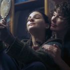 Zwei Personen sitzen eng beieinander, die jüngere hält einen Spiegel, sie wirken nachdenklich und geborgen.