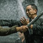 Zwei Männer kämpfen im Regen; einer hält ein Stöckchen, während er den Schlag des anderen abwehrt.