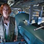 Eine Frau mit roten Haaren steht in einem futuristischen Labor voller Geräte und Bildschirmen.