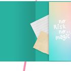 "No risk no magic" in weißer Schrift auf einem pastellfarbenen Hintergrund. Daneben ein offenes Notizbuch mit Papier.
