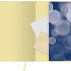 Ein blassgelbes Papier mit einem linierten Blatt und einem beige Zettel, daneben blaues Bokeh-Muster.