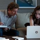 Zwei Personen arbeiten konzentriert an einem Laptop und machen Notizen, auf einem Sofa sitzend.