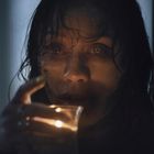 Ich kann keine Texte oder deren Details erkennen. Eine Frau mit nassen Haaren hält ein Glas mit Kerze.
