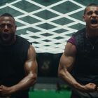 Zwei muskulöse Männer schreien energisch. Einer trägt ein Nike-Logo auf dem Shirt. Hintergrund mit leuchtendem Muster.