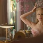 Ich kann nicht erkennen, wer die Person ist. Eine Frau im rosa Kleid setzt sich eine funkelnde Krone auf. Innenraum mit Lampe.