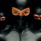 Drei Personen in schwarzen Ganzkörperanzügen, die Augen fokussieren direkt und intensiv.