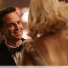 Ein Mann in einem Anzug lächelt eine Frau mit blonden Haaren an, während sie sich unterhalten.