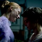 Zwei Personen stehen sich nahe gegenüber. Eine trägt ein lila Kleid, die andere ein gestreiftes Shirt. Es ist dunkel.