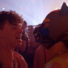 Ein junger Mann in einem Club, ein anderer trägt eine Maske mit Tierohren und einem Gitter vor dem Mund.