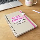 Kladde mit Text: "KEINE AHNUNG Ich arbeite hier nur." Daneben Laptop, Tasse und Stift auf Holzfläche.