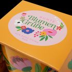 Text: "Bunte Blumengrüße", "New Bone China Mug". Runde, bunte florale Illustration auf einem gelben Hintergrund.