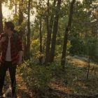 Eine Person im karierten Hemd wandert bei Sonnenuntergang durch einen dichten Wald, umgeben von Bäumen und Blattwerk.
