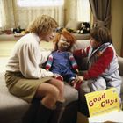 Text: „Good Guys“. Eine Frau und ein Kind sitzen neben einer rothaarigen Puppe auf einem Sofa. Spielzeug ist herum verstreut.