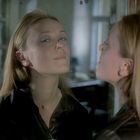 Eine Frau betrachtet ihr Spiegelbild in einem leicht verschwommenen Spiegel, ihr Gesichtsausdruck wirkt nachdenklich.