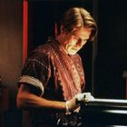 Es gibt keinen sichtbaren Text. Ein Mann in gemustertem Hemd konzentriert sich bei schwacher Beleuchtung auf eine Schreibmaschine.