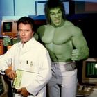 Ein Mann in weißem Kittel mit einem Klemmbrett steht neben einer großen grünen Figur mit wütendem Gesichtsausdruck.